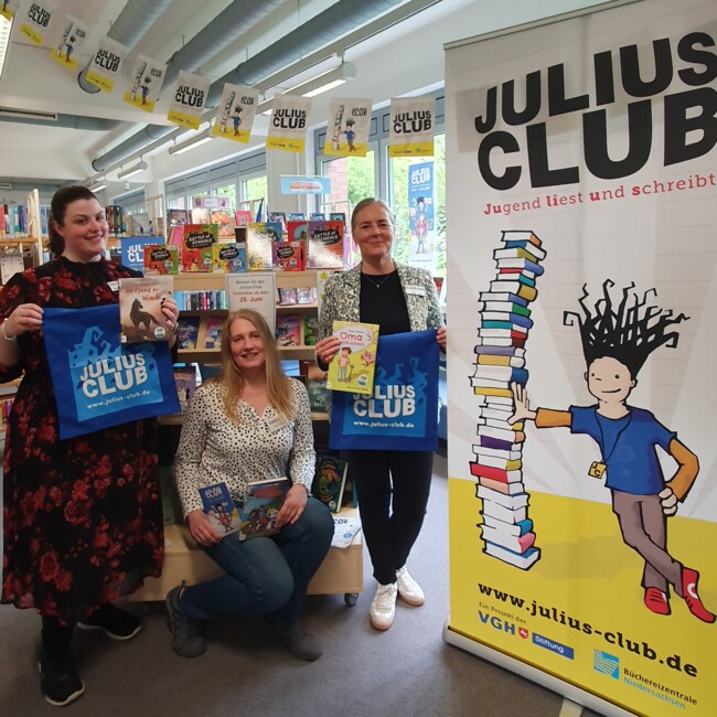 Foto mit Mitarbeiterinnen, die auf den Julius Club hinweisen